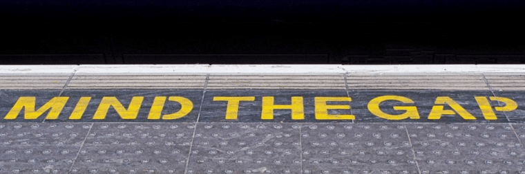 The phrase "Mind the Gap" is painted on the concrete of a street.
